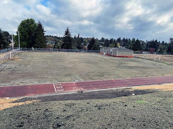 a field and track has portables in one corner and green-gray material on dirt